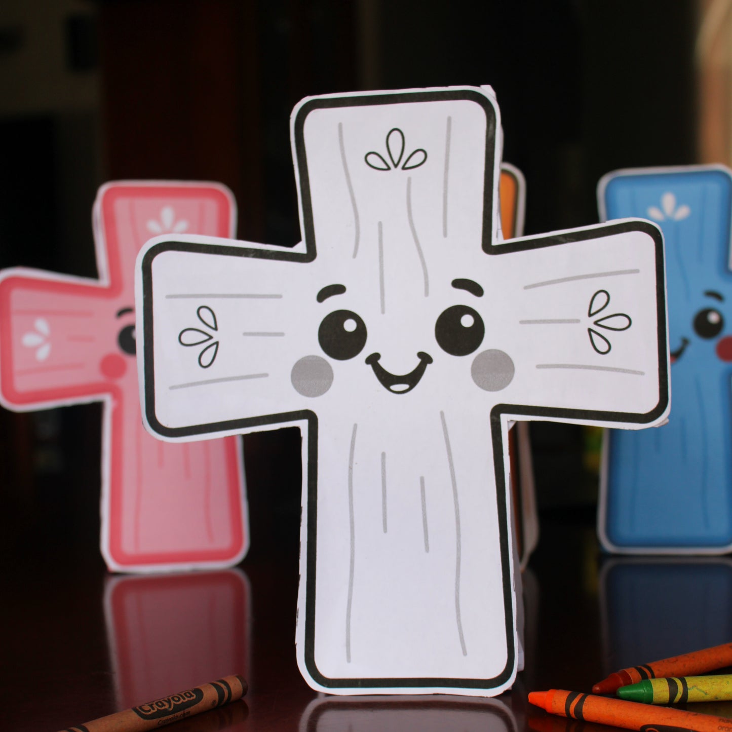 Cross-shaped character coloring craft with a smiley face design on a reflective surface.