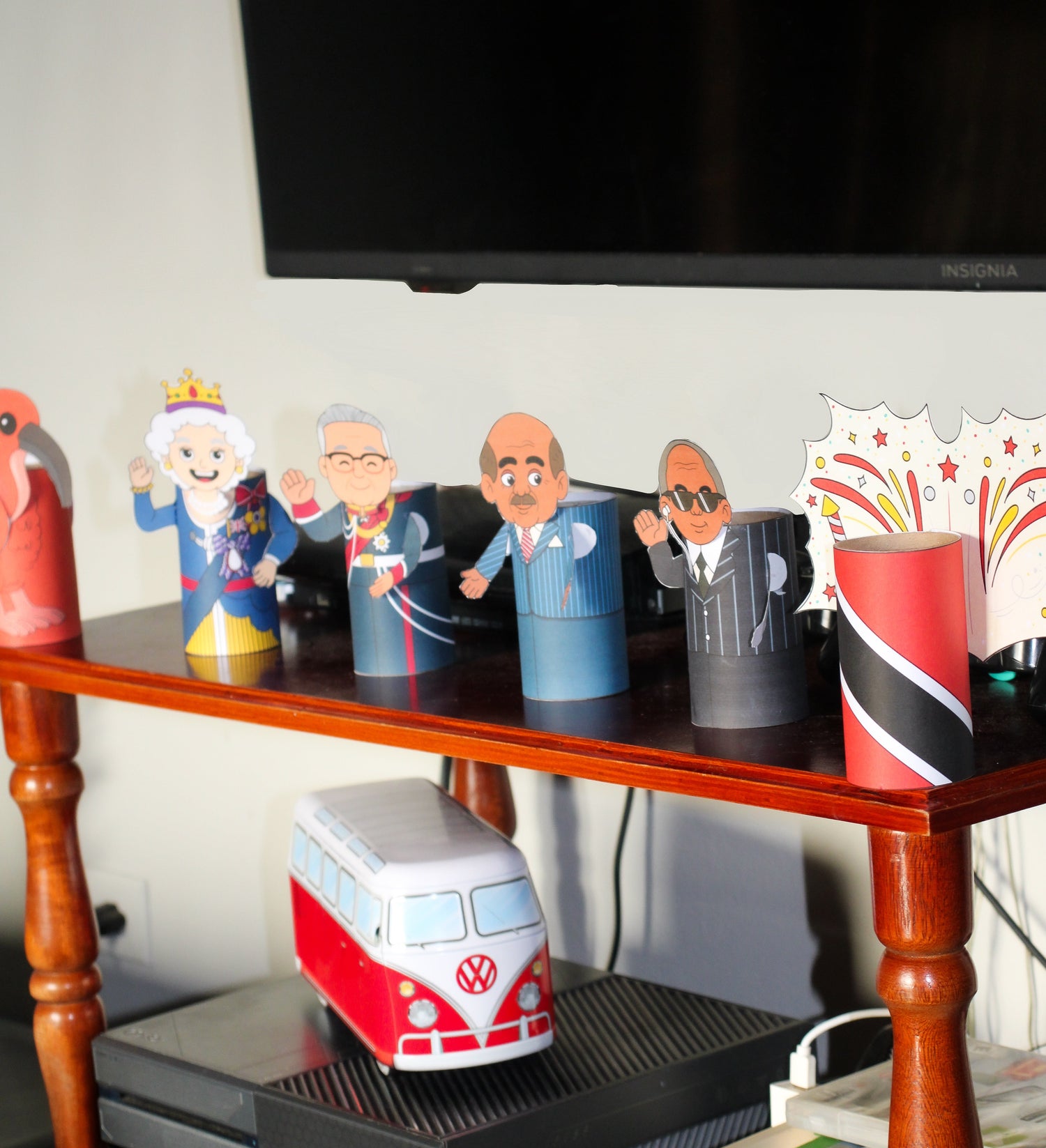 Collection of important Trinidad and Tobago figurines and a Volkswagen van-shaped object on a wooden shelf with a TV in the background.