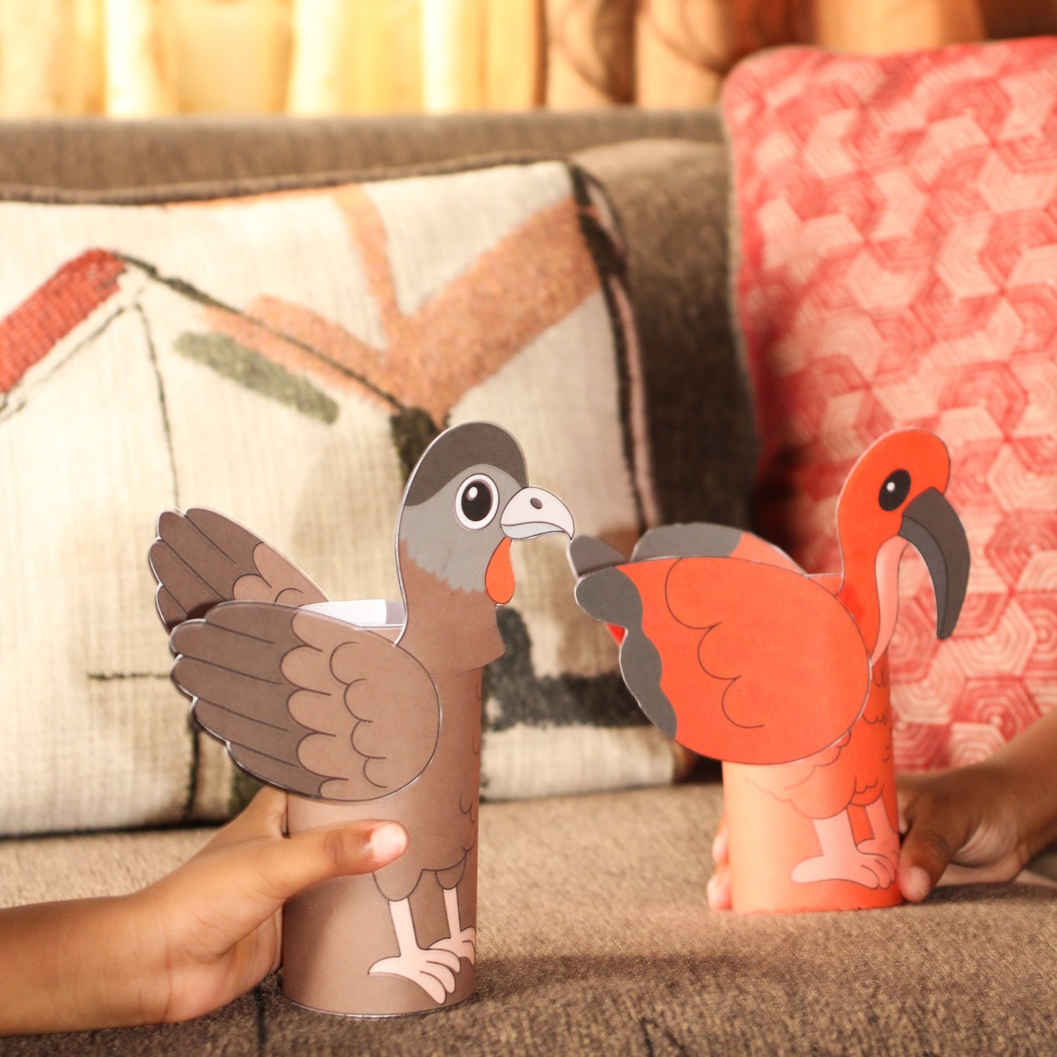 Two paper roll animals, one brown and one orange, on a couch with a blurred background.