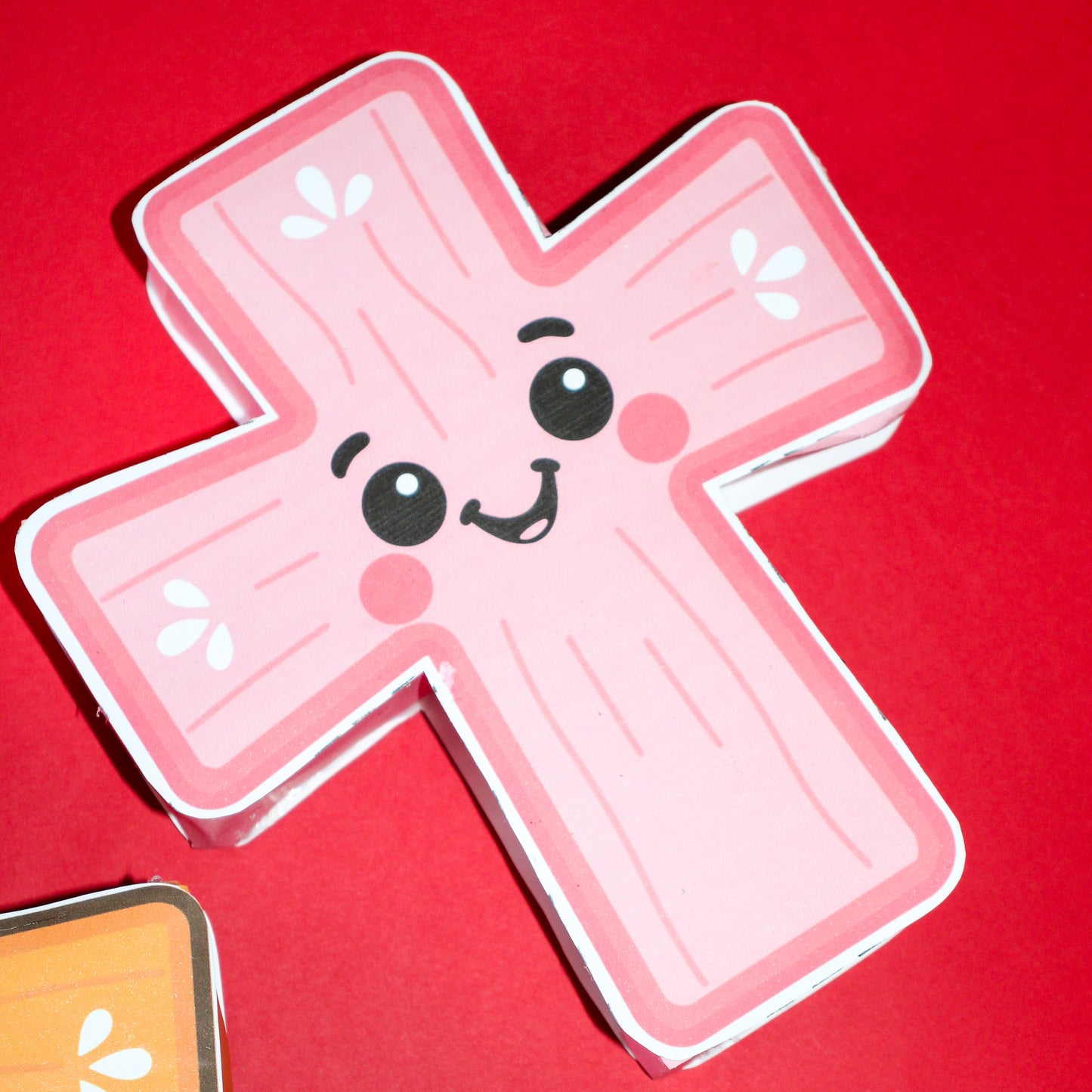 Pink papercraft cross-shaped character with a smiley face on a red background